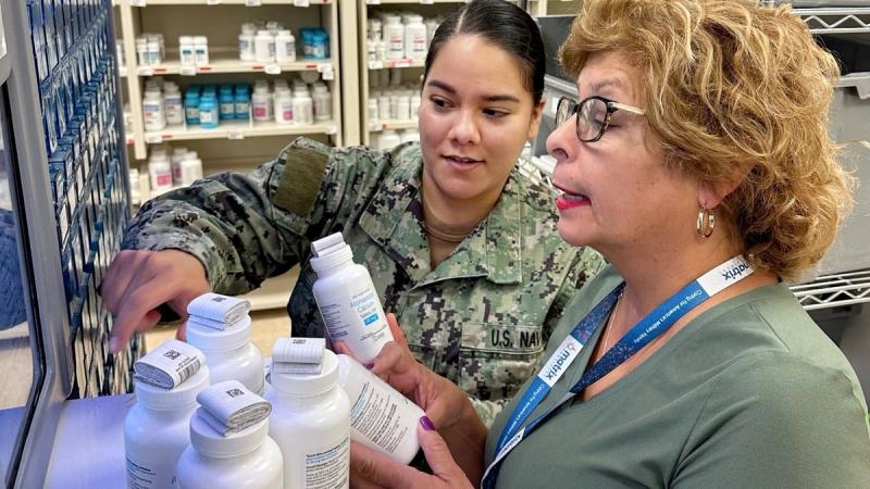 Hospitalman Jacqueline Diaz instructs Rose Villarreal, both pharmacy technicians at Naval Hospital Jacksonville pharmacy, on how to fill the medicine dispenser.