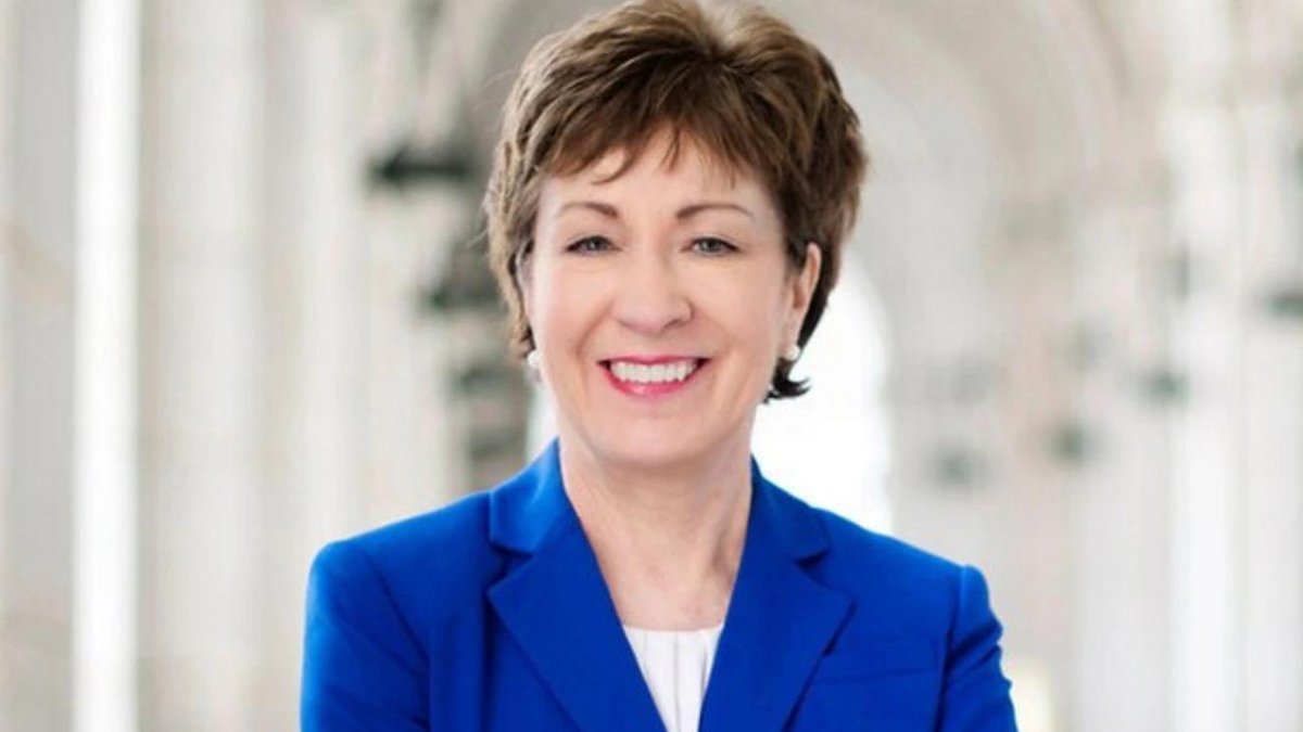 Senator Susan Collins smiling in a blue blazer, standing in a hallway.