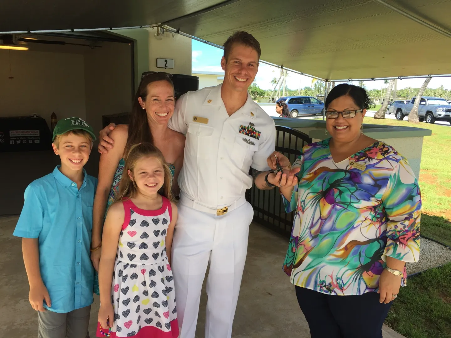 A Navy chief petty officer in dress whites with his wife and two children receives house keys from a housing office representative