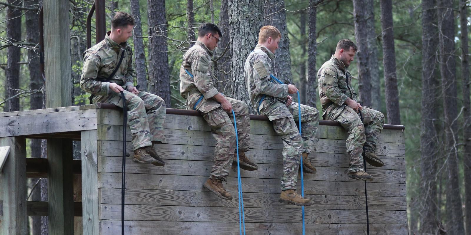 Four soldiers sit atop of a wooden wall.