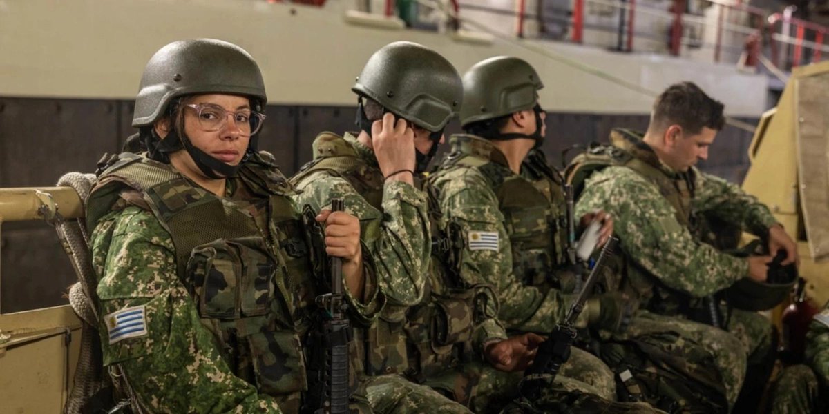 Soldiers in camouflage uniforms and helmets seated inside a military vehicle.