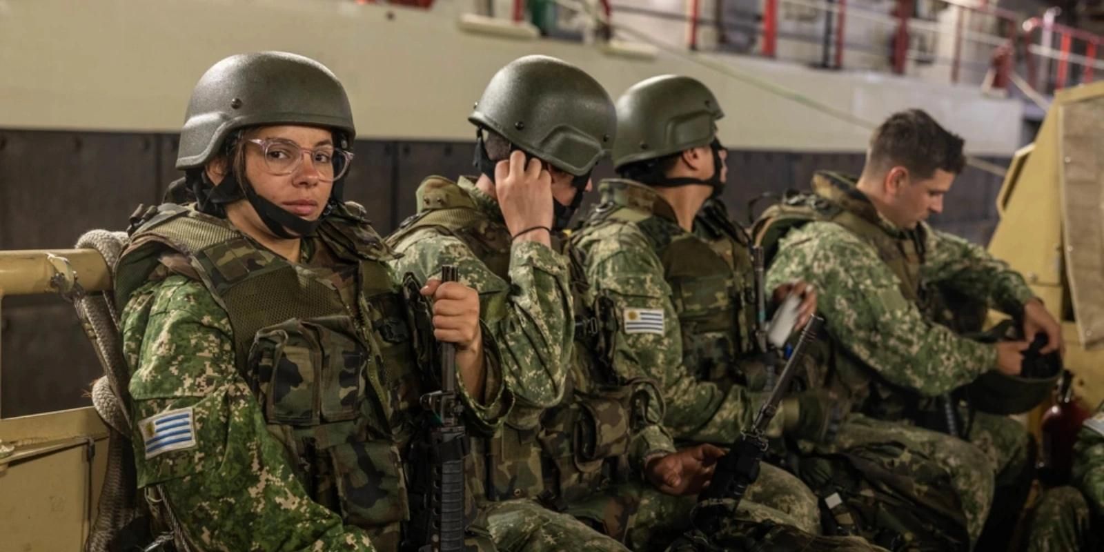 Soldiers in camouflage uniforms and helmets seated inside a military vehicle.