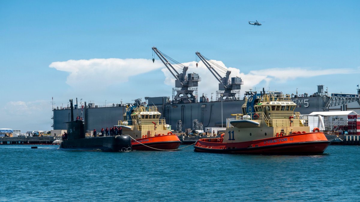 Two tugboats and a battleship in a harbor.