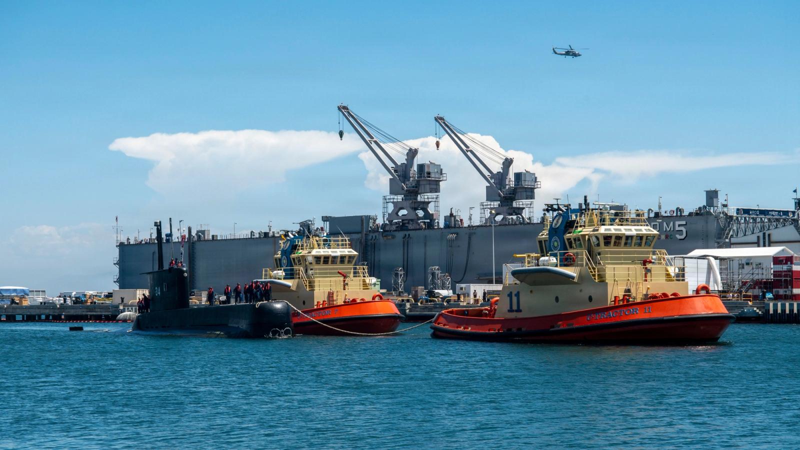 Two tugboats and a battleship in a harbor.