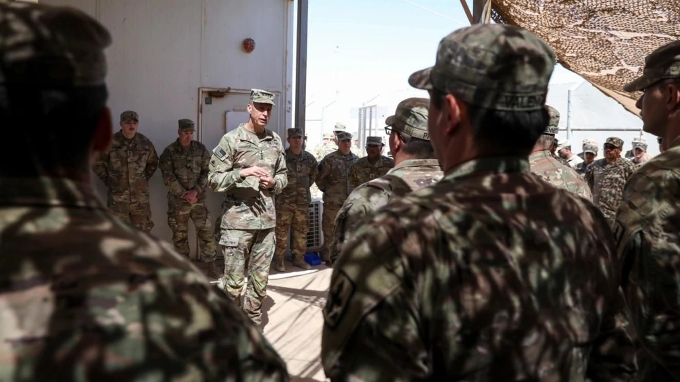 Air Force officer addressing airmen in camouflage uniforms at military base assembly