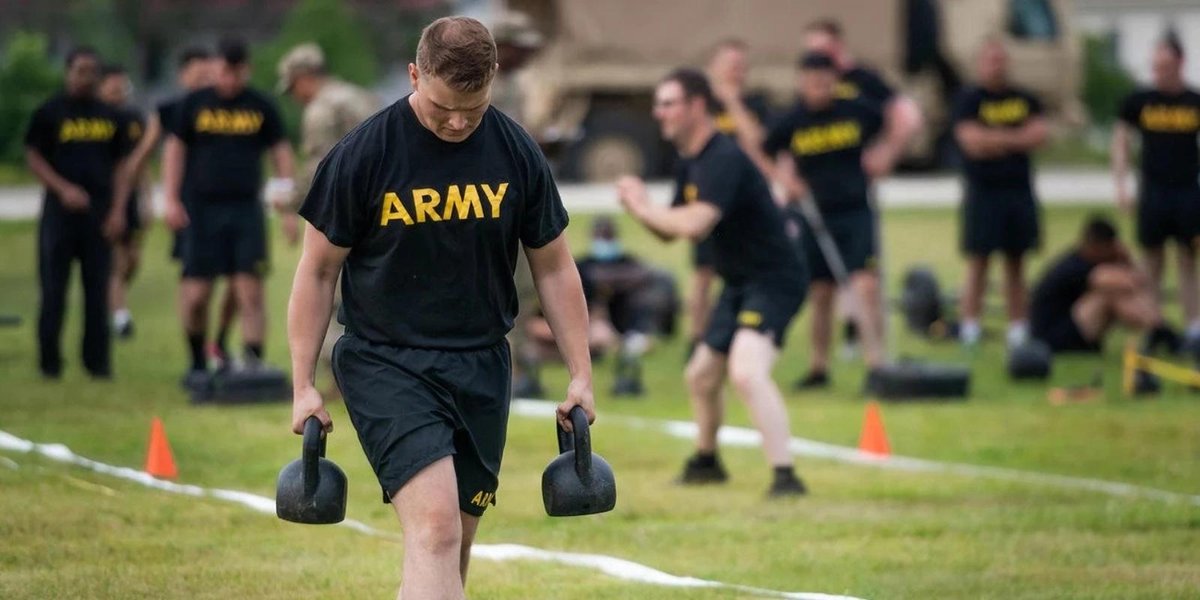 Army soldiers in PT uniforms lifting kettlebells during outdoor training session.