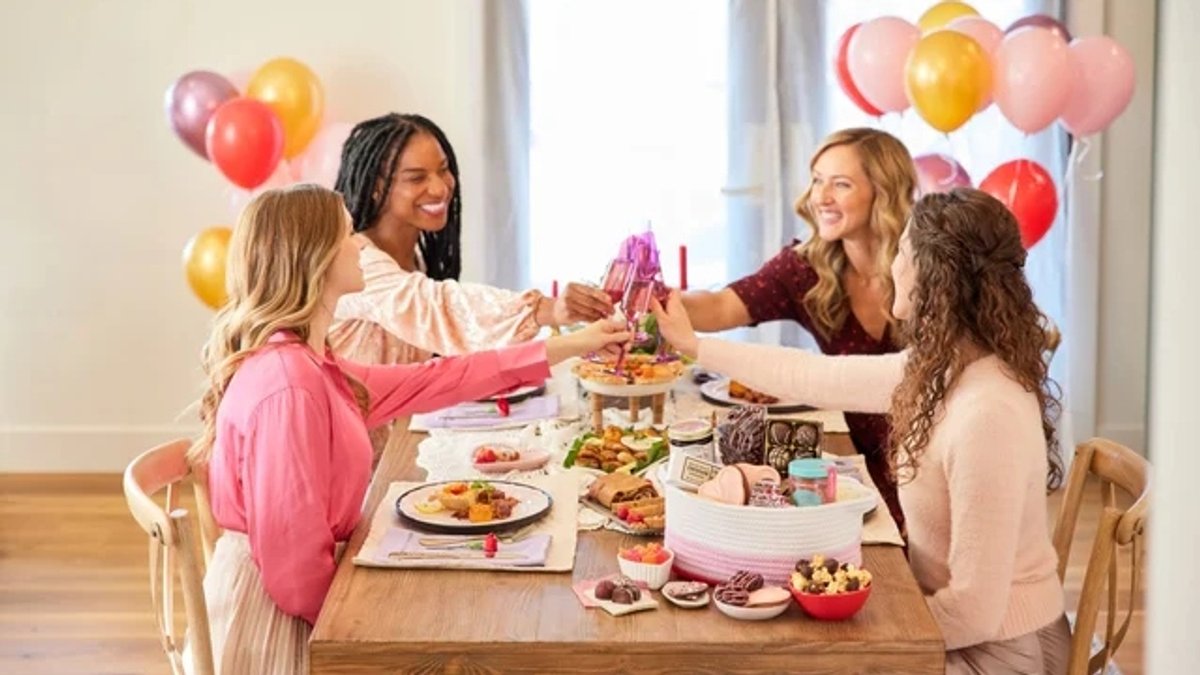 Four women share a toast around a festive table.