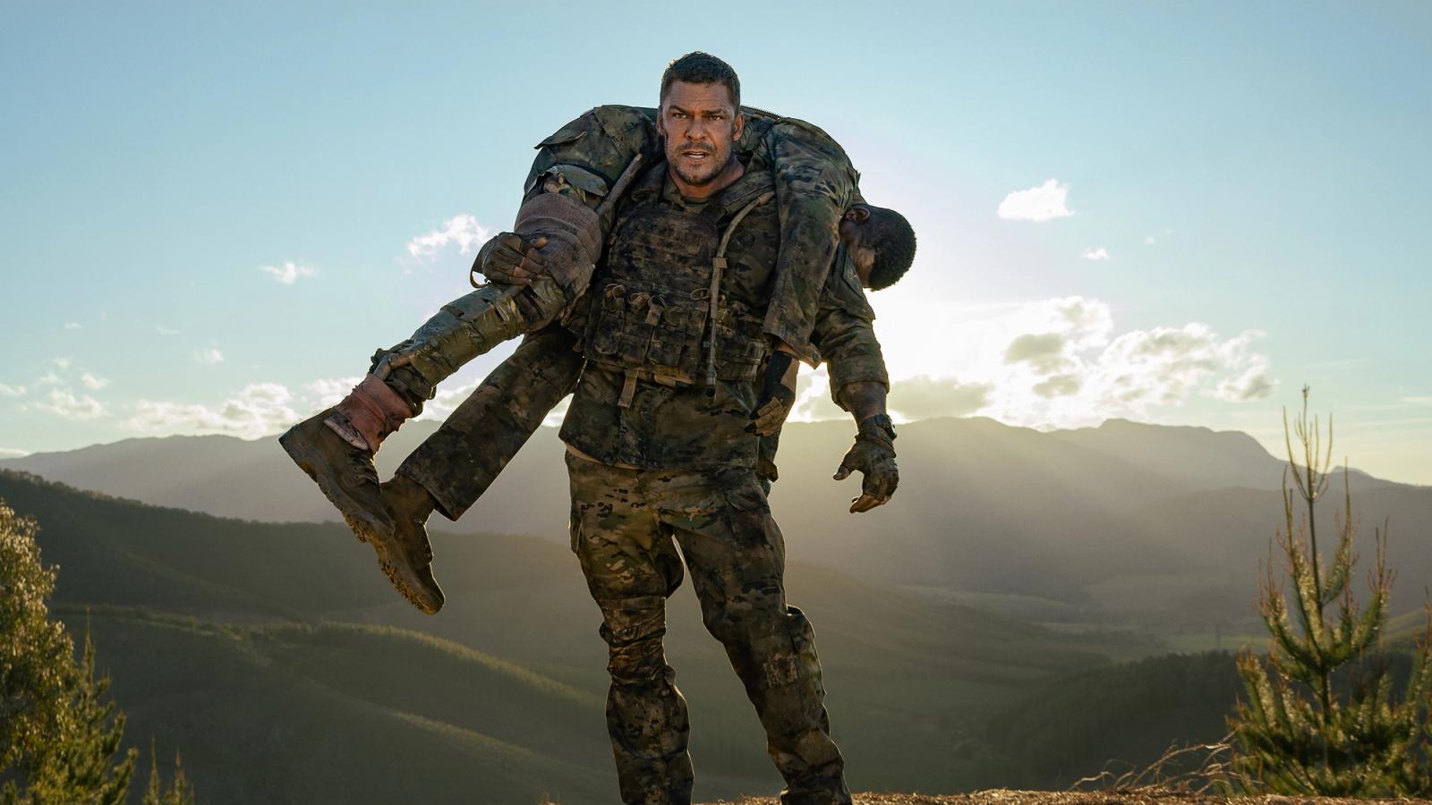 Alan Richson carries another soldier, standing on hill.