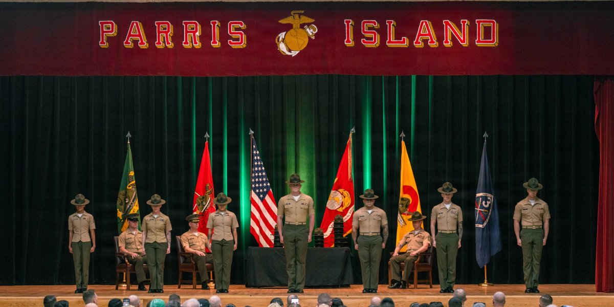 Uniformed Marines stand on a stage during graduation at Parris Island.