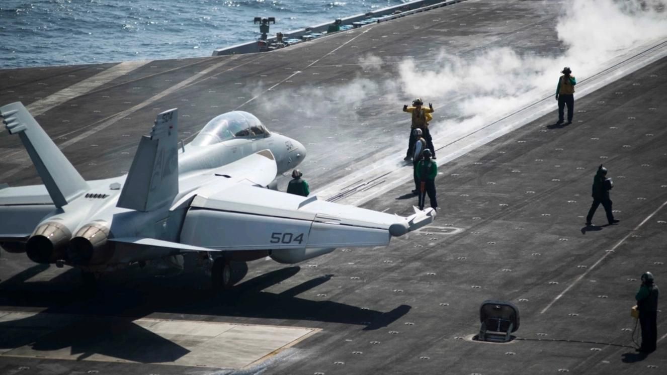 EA-18G Growler on aircraft carrier deck preparing for takeoff, crew members nearby
