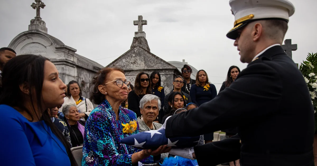 A wife is handed a flag at a military funeral.