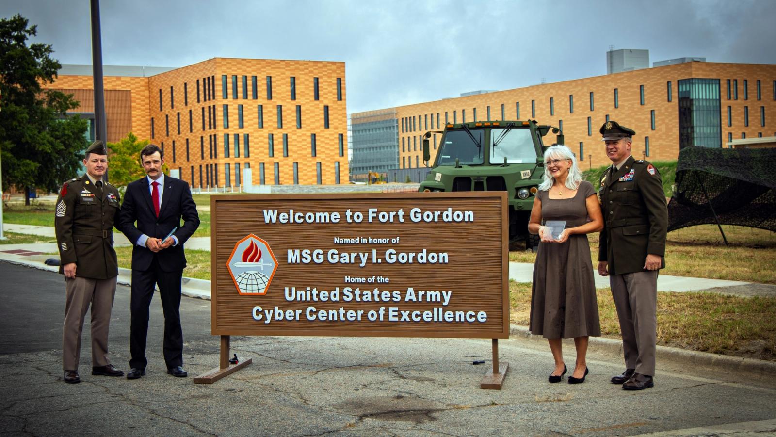 Officers and civilians stand in front of a sign for Fort Gordon.