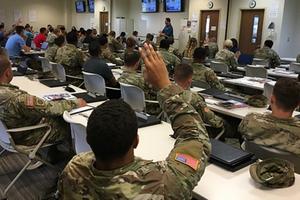 Uniformed soldiers sit in a classroom with a hand raised.