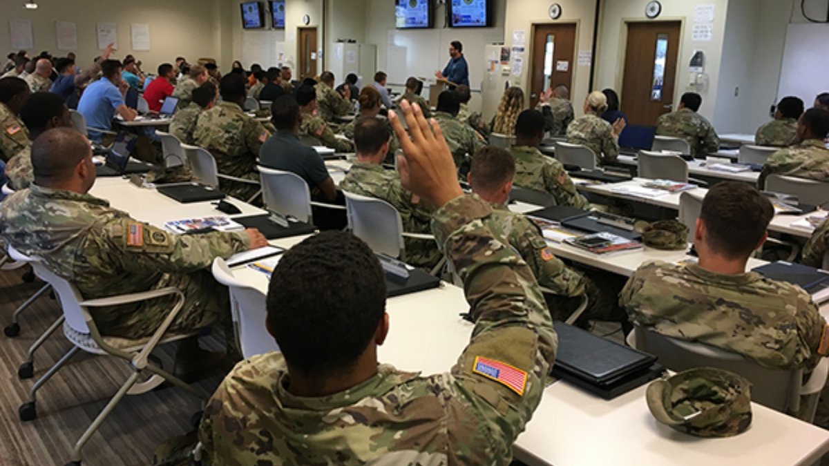 Uniformed soldiers sit in a classroom with a hand raised.