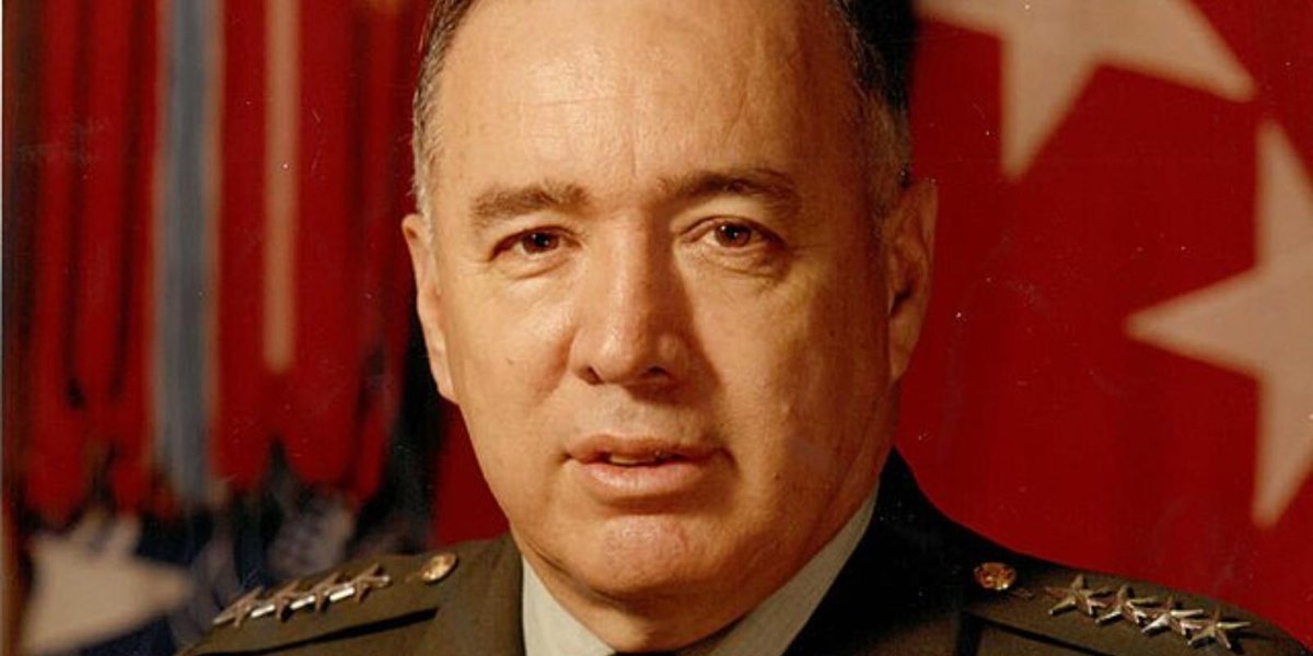 Army General in uniform with military decorations and flag backdrop.