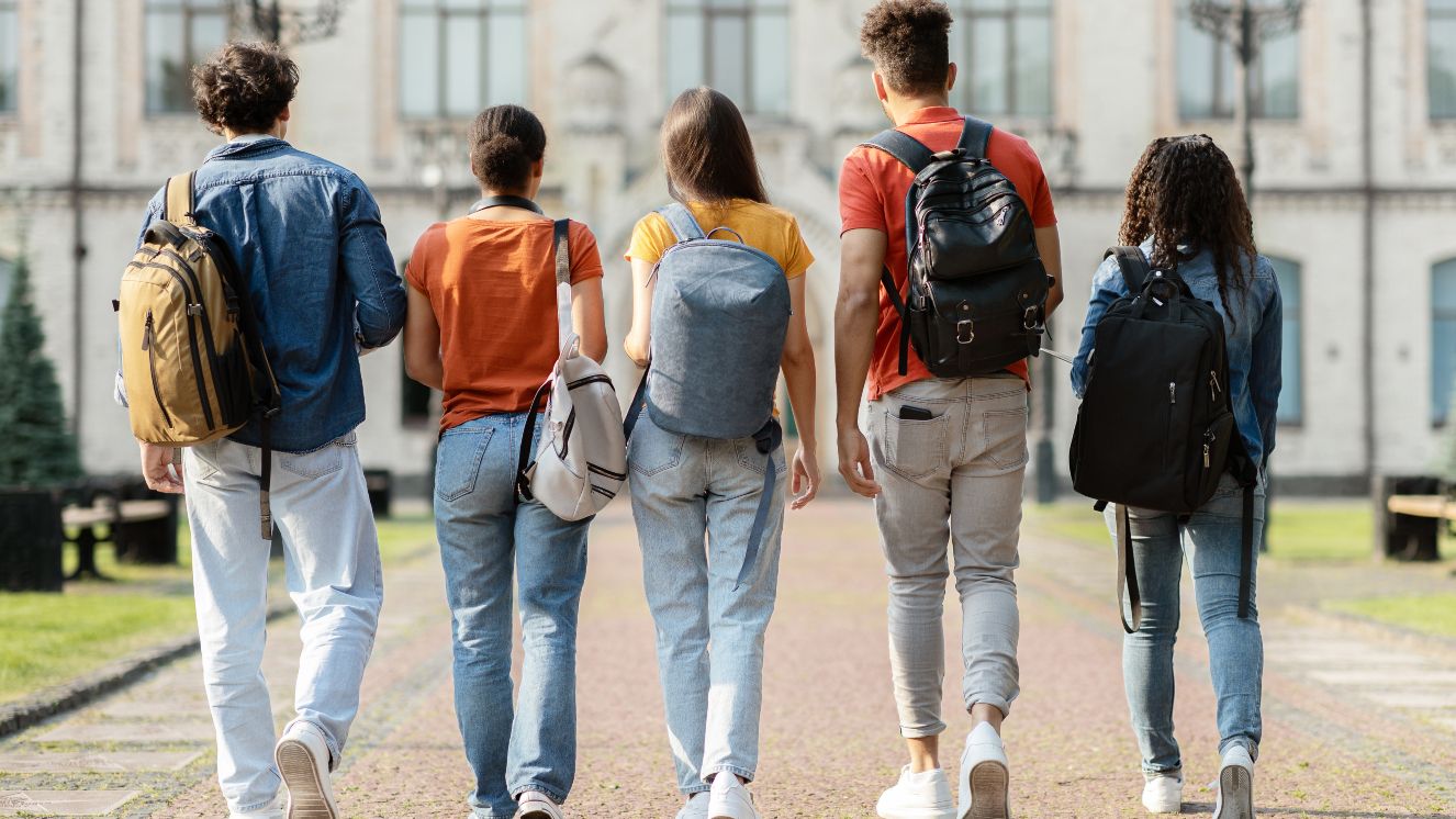 Group of five students with backpacks walking at university campus together.