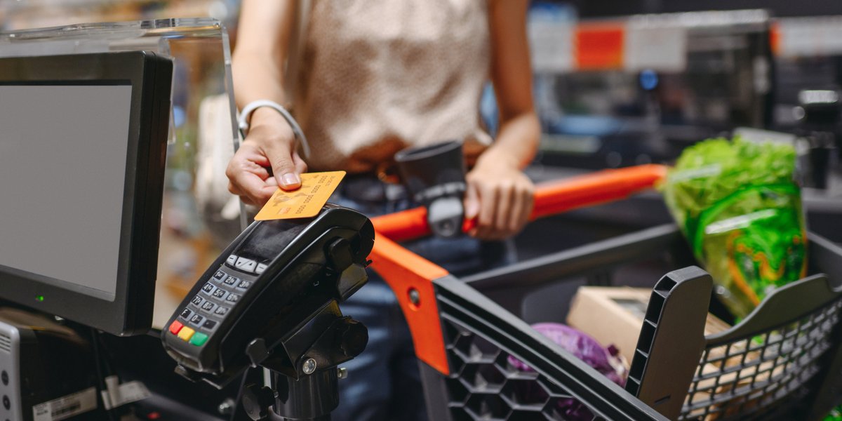 Person using a credit card at grocery store checkout with produce in cart