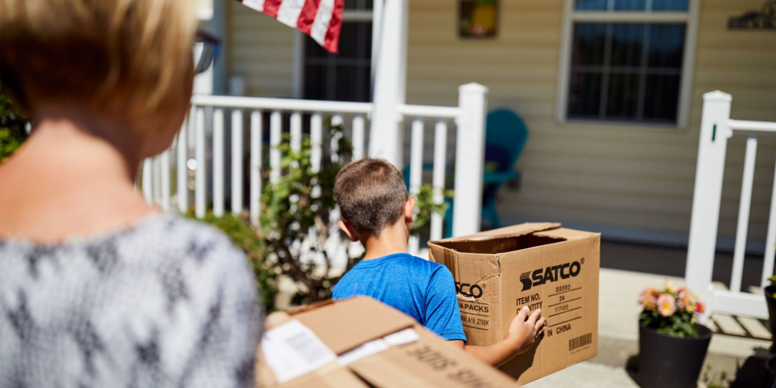 A mother and her son move out of their home, carrying boxes.