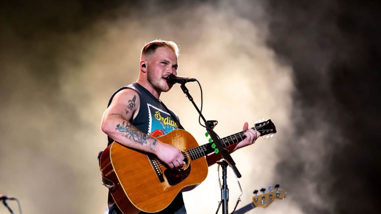 Country musician performing with guitar on stage under spotlight.