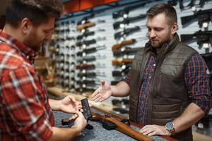 A salesman talks to a customer holding a gun in a gun shop.