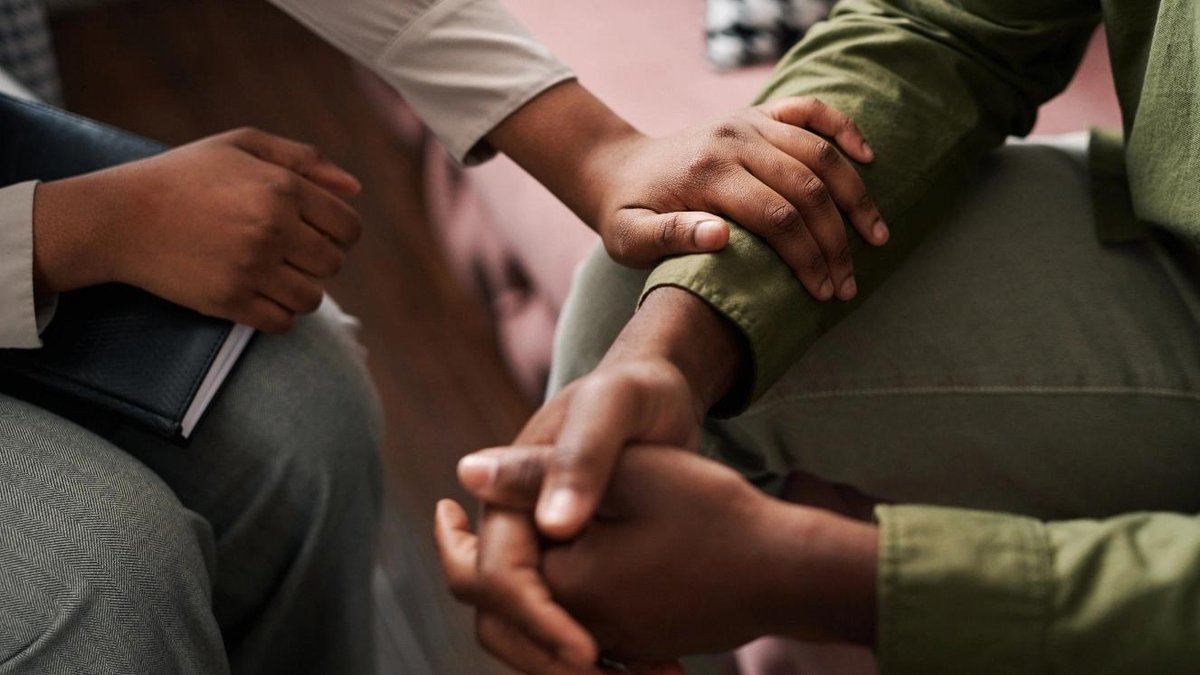 Veteran receiving supportive counseling, hands clasped with therapist in office setting.