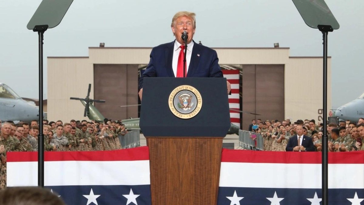 Trump speaking at military base with troops and American flag backdrop