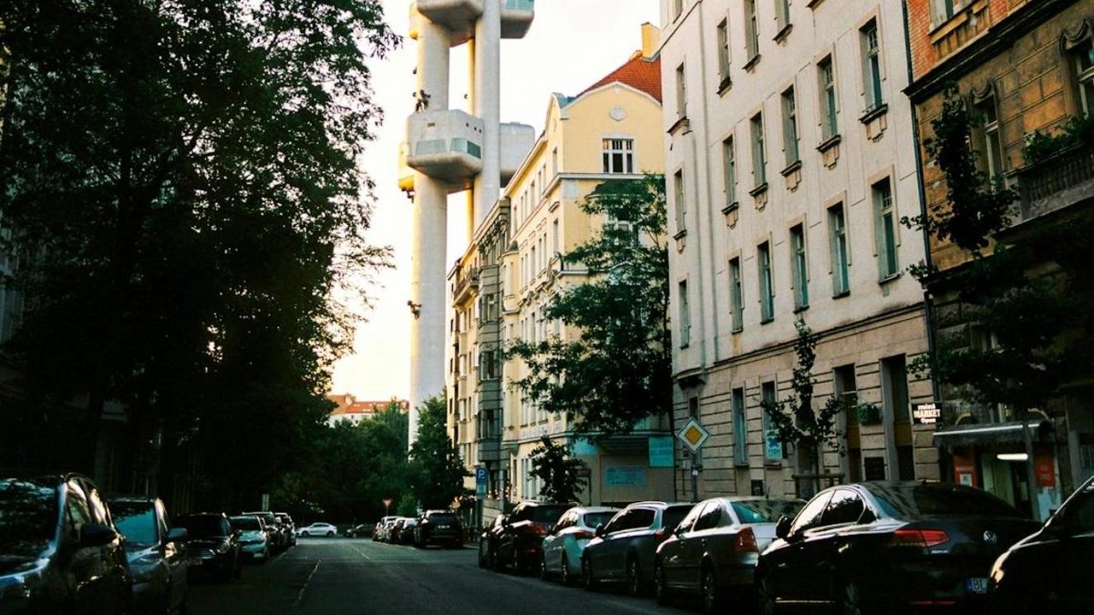 Street view with parked cars and a unique tall building structure in the background.