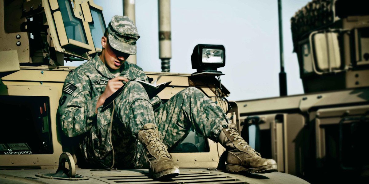 A soldier sits on a car and writes a note.