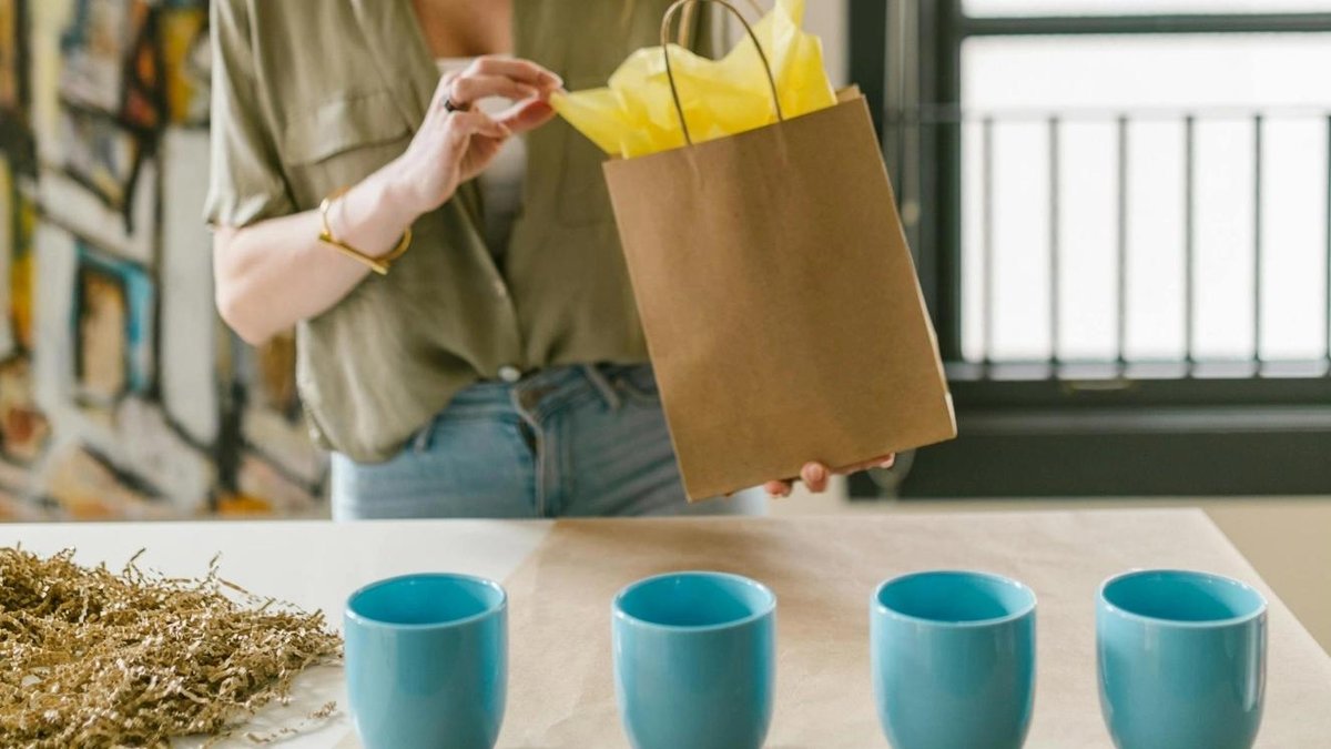 Veteran arranging yellow tissue paper in gift bag beside blue mugs on table