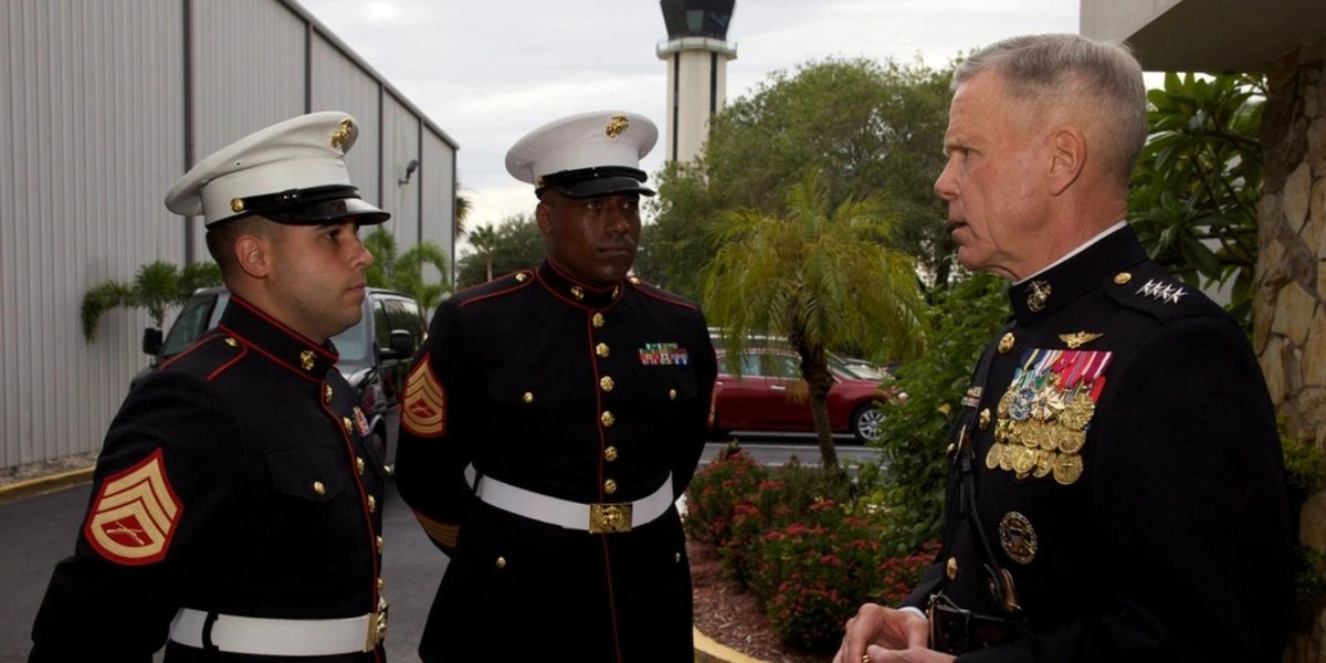 Marine Corps officer awarding honorary Marine titles to two sergeants outside a military facility.