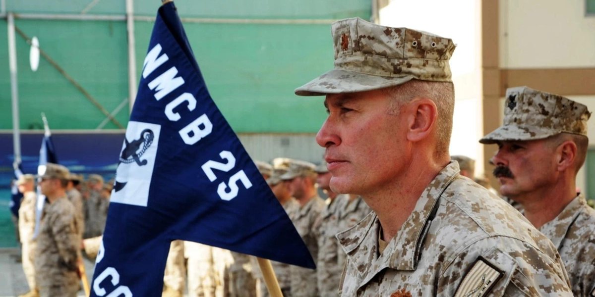 Navy Reserve officer in uniform holding NMCB 25 flag during formation.