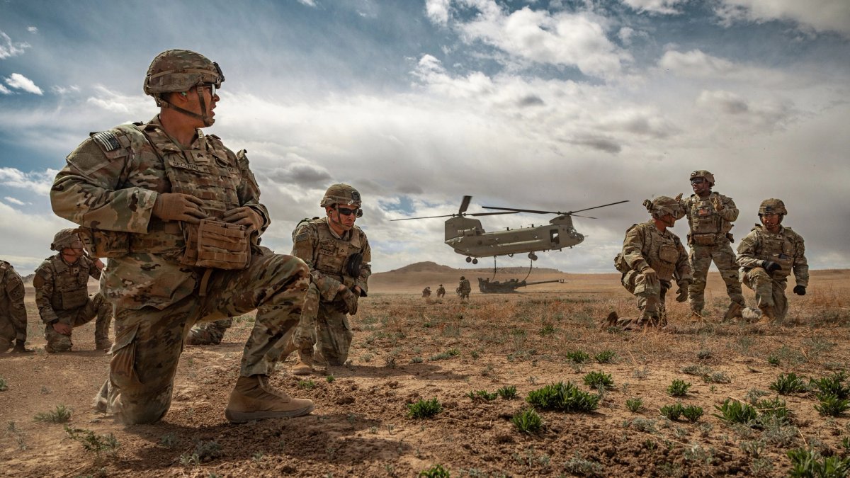 Uniformed servicemen watch a helicopter landing while in training for combat.