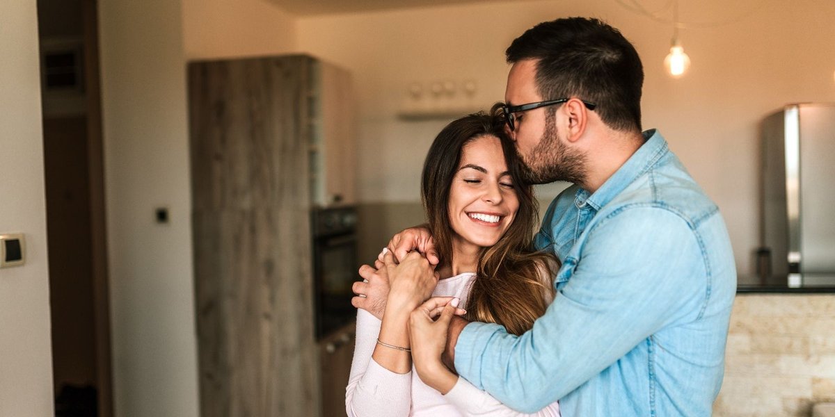 Veteran embracing partner in a modern kitchen, smiling together.