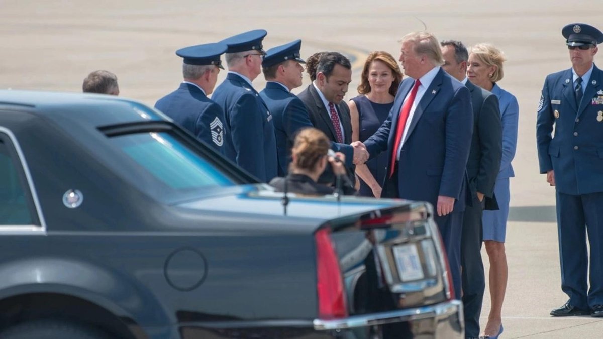 Trump greeting military personnel and officials on airport tarmac near black vehicle