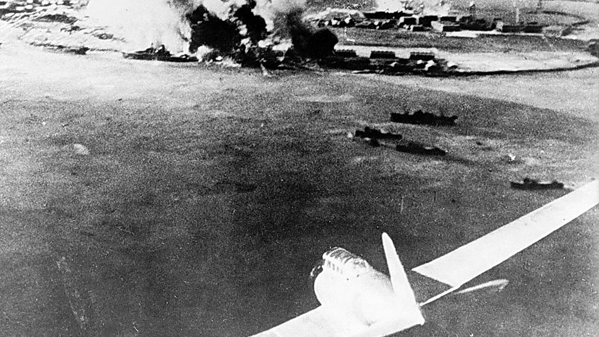 Japanese aircraft over Pearl Harbor during the 1941 attack, smoke rising from battleships below.