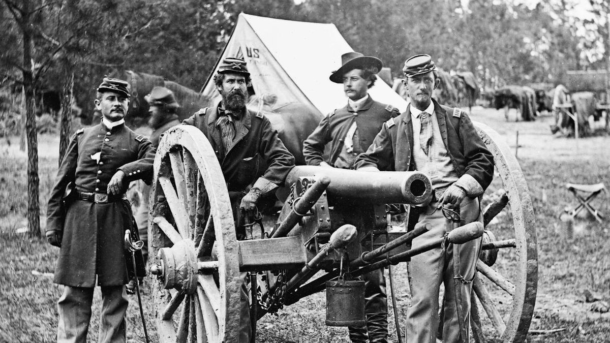 Union soldiers standing by a Civil War-era cannon with tents in the background