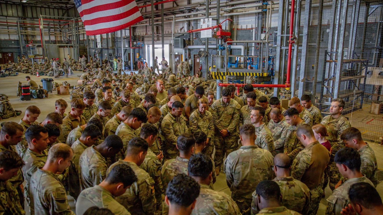 A large group of servicemembers stand and pray.