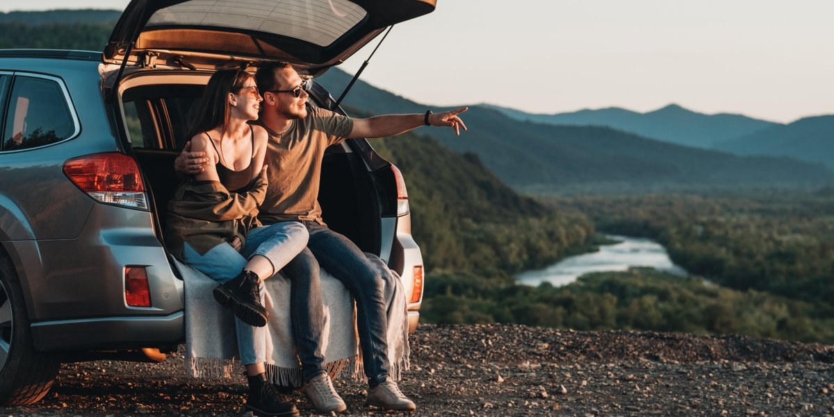 Man and a woman sit in the hatchback of a car as the man points to the horizon.