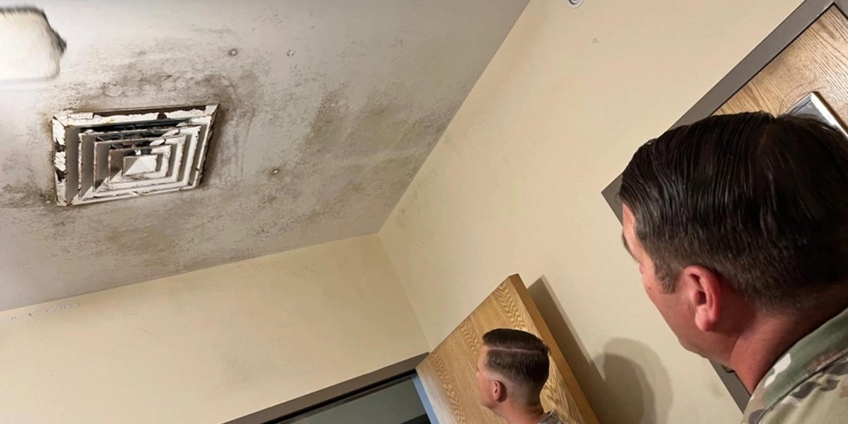 Soldier inspecting mold-infested ceiling near air vent in Hunter Army Airfield housing.