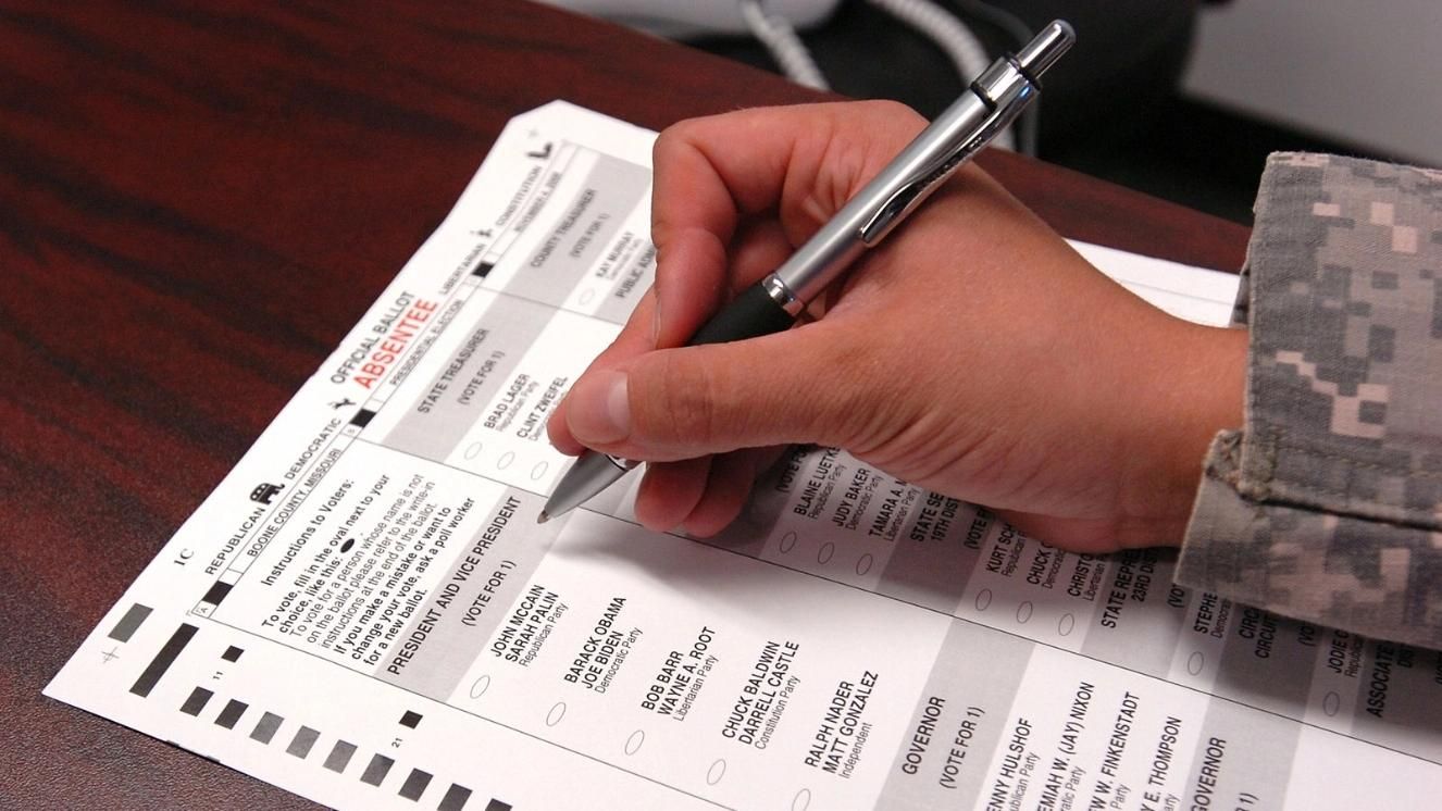Military personnel in camouflage filling out absentee ballot form