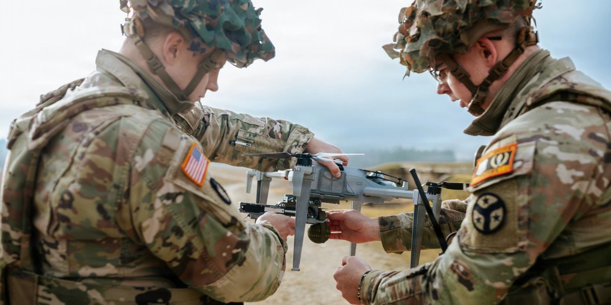 Two uniformed men make adjustments on a drone.
