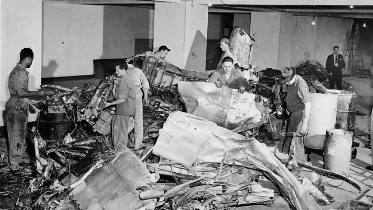 Workers examining wreckage from the 1945 B-25 Empire State Building crash in building interior.