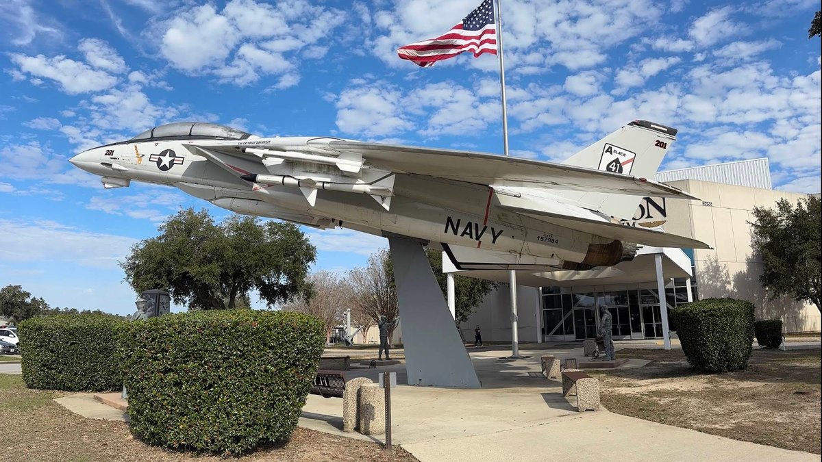 A navy jet sits on a pedestal in an aviation park.