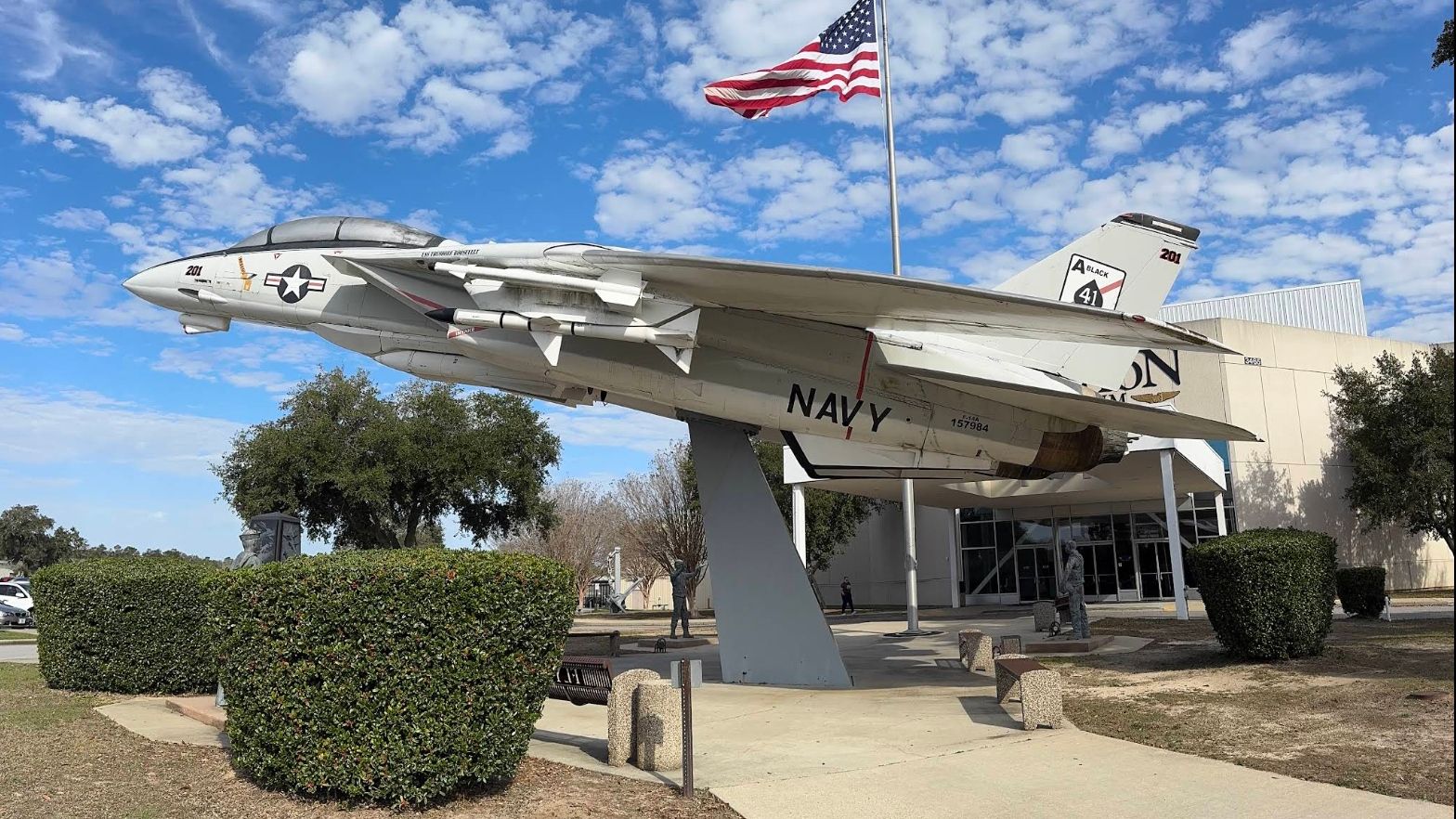 A navy jet sits on a pedestal in an aviation park.