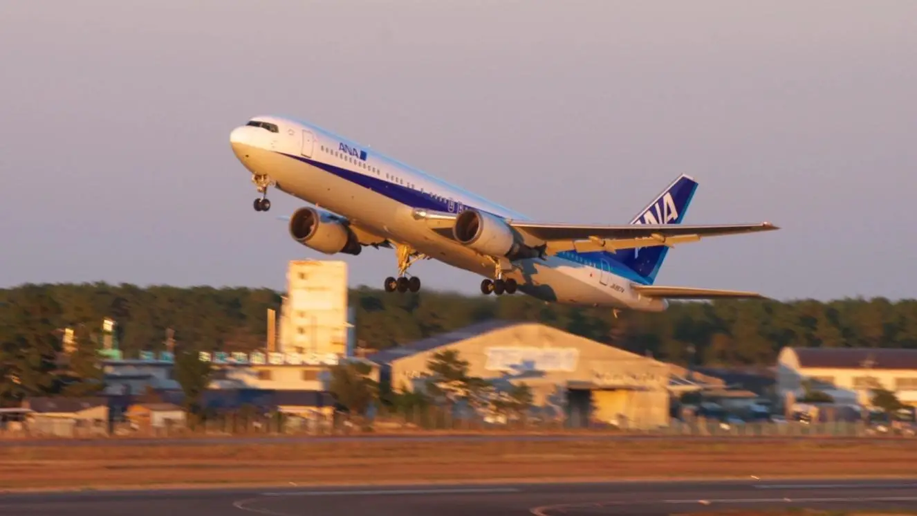 ANA commercial airplane taking off from Miyazaki Airport runway at sunset.