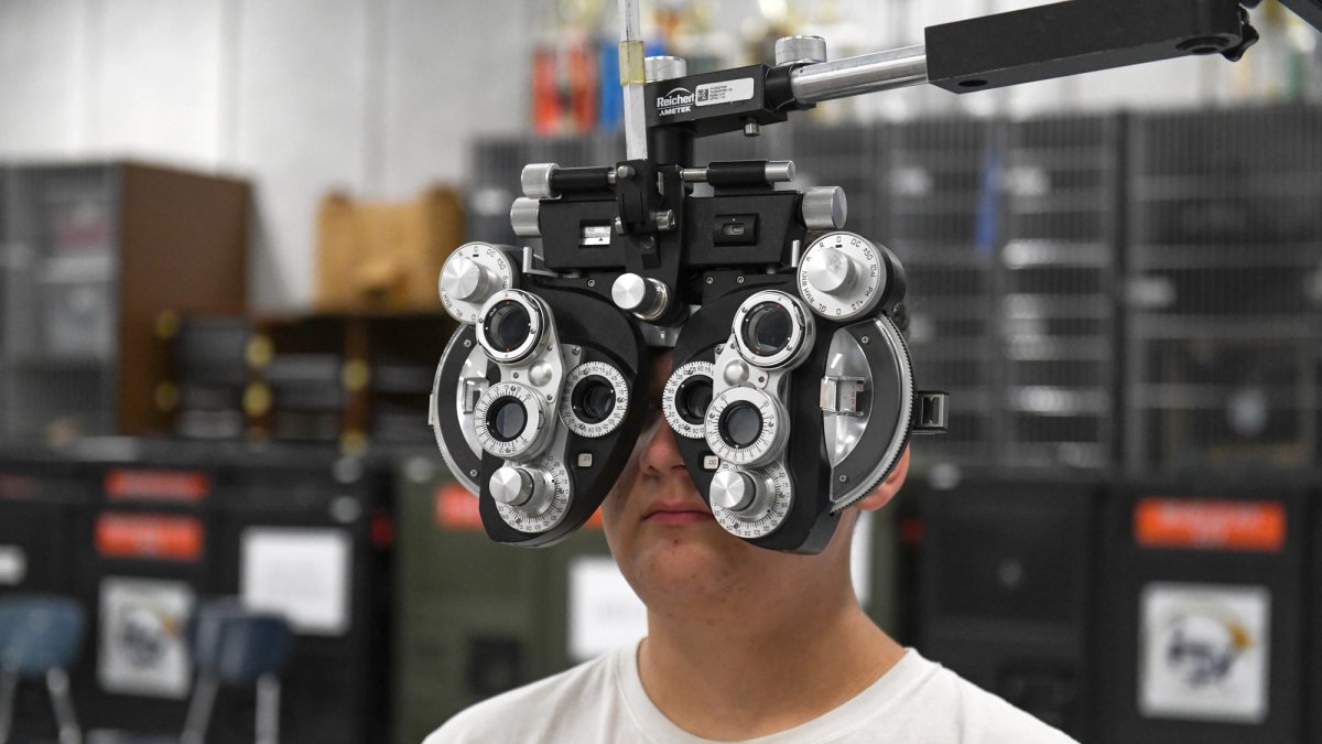A man is seen behind an eye exam instrument with about a dozen lenses.