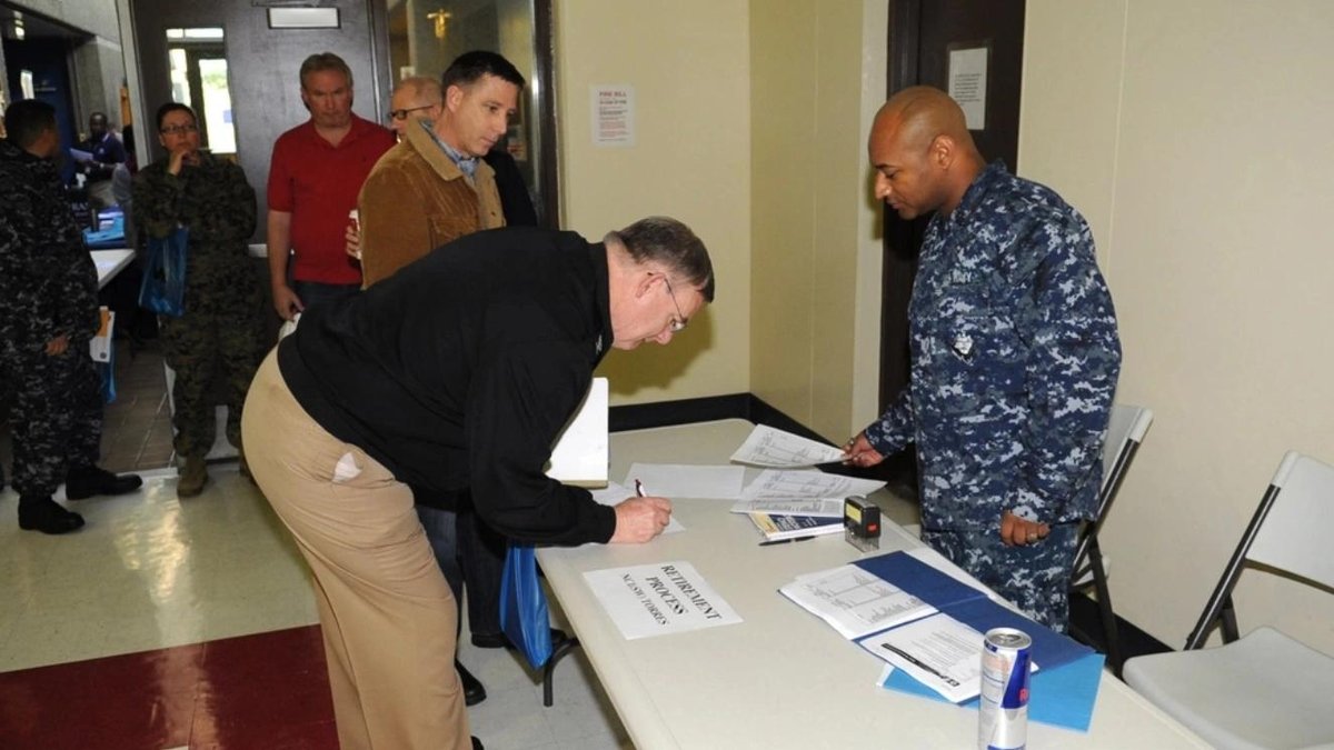 Navy personnel assisting veterans at benefits information desk in hallway