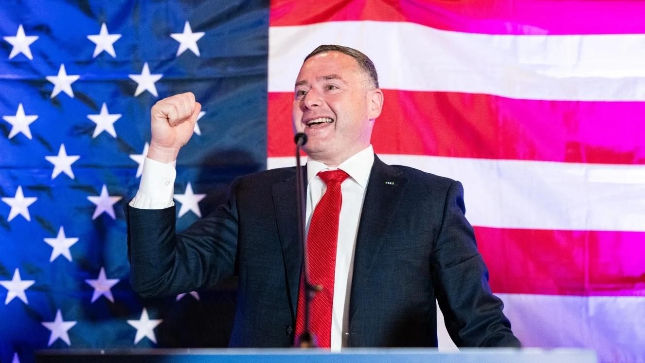 Eugene Vindman speaking at podium with American flag backdrop