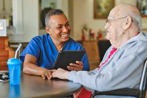  A med worker in scrubs talks to a senior man.