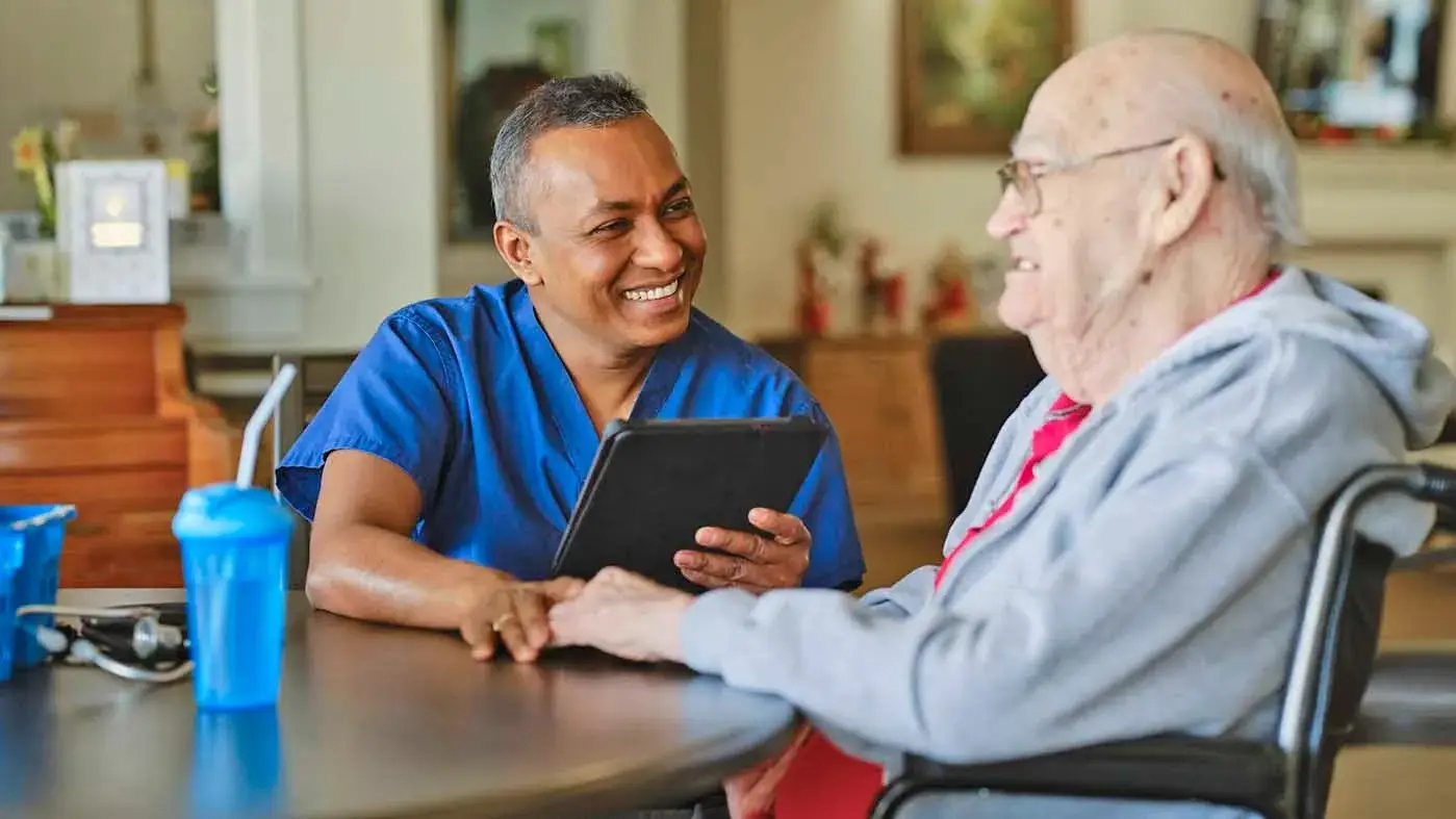 A med worker in scrubs talks to a senior man.